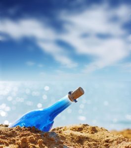 5751014 - blue glass bottle in sand and airy clouds like genie